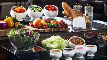A buffet table with various food items including salads, fruits, vegetables, bread, and condiments.