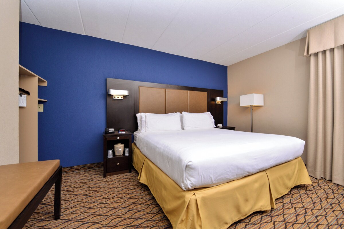 A hotel room with a bed, bedside tables, a desk, and a lamp.