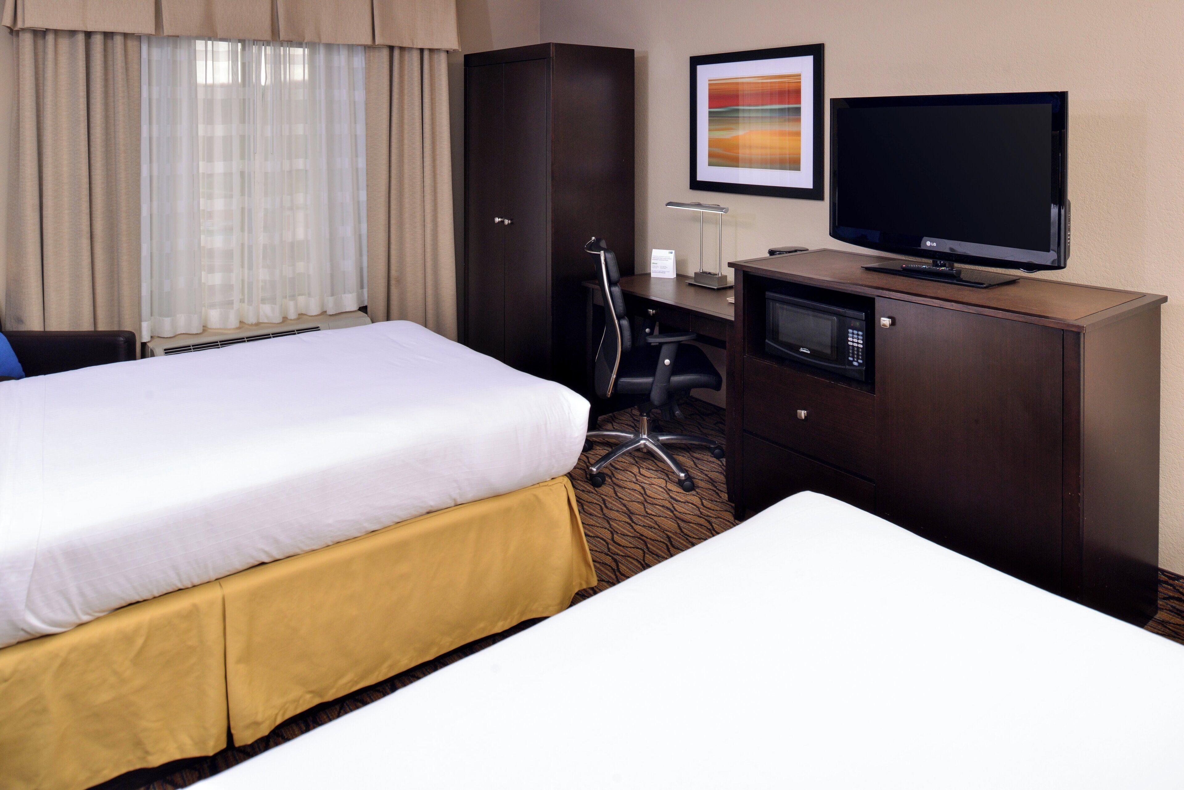 A hotel room with a bed, a desk with a television, a wardrobe, and a chair.