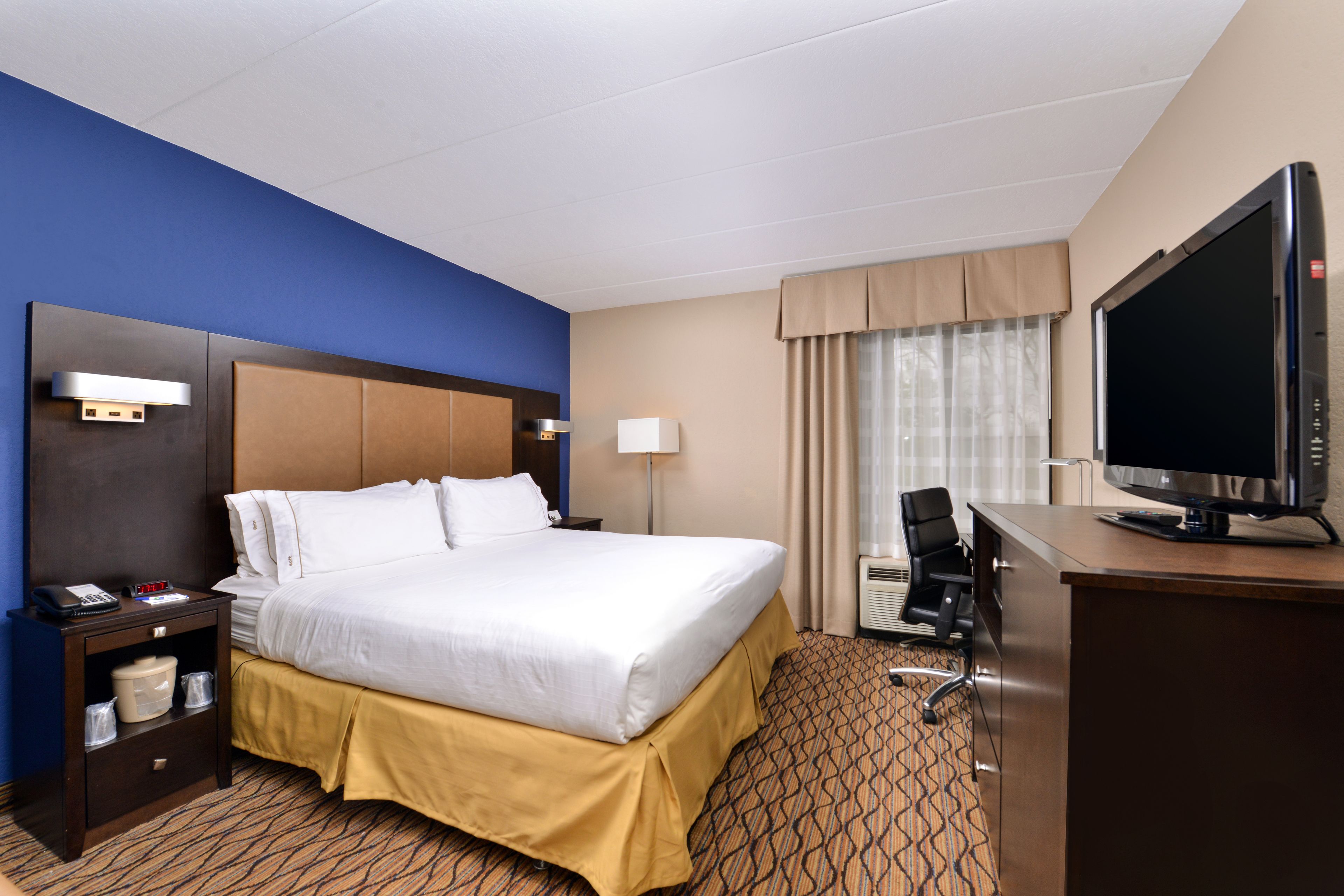Une chambre d’hôtel avec un grand lit, un bureau avec une télévision, une chaise, une table de chevet et une lampe.