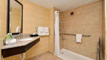 Un baño moderno con lavamanos de granito, un espejo grande, ducha a ras de suelo con puerta de vidrio y un perchero para toallas.