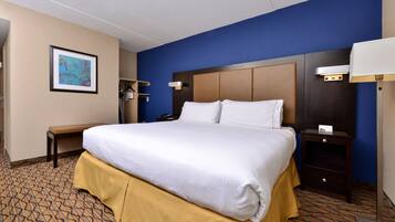A hotel room with a large bed, a bedside table, a nightstand, a bench, and a framed picture on the wall.