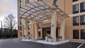 A hotel entrance with a covered patio, potted plants, and a bench. - Holiday Inn Express Hunt Valley by IHG (Hunt Valley)