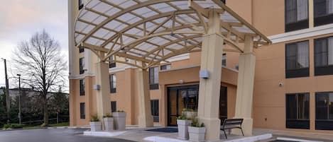 A hotel entrance with a covered patio, potted plants, and a bench.