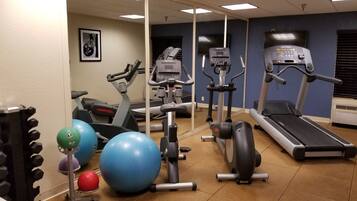 Une salle de sport équipée de divers appareils, notamment des tapis de course, un vélo elliptique et des ballons d’exercice.