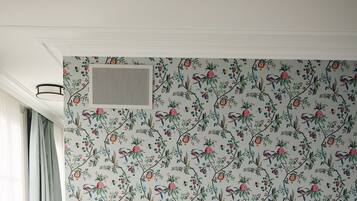A neatly made bed with white linens, a wooden nightstand with a lamp, and a floral wallpaper pattern.