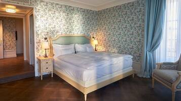 Un dormitorio con una cama grande, dos mesitas de noche con lámparas, papel tapiz con motivos florales y suelo de madera.