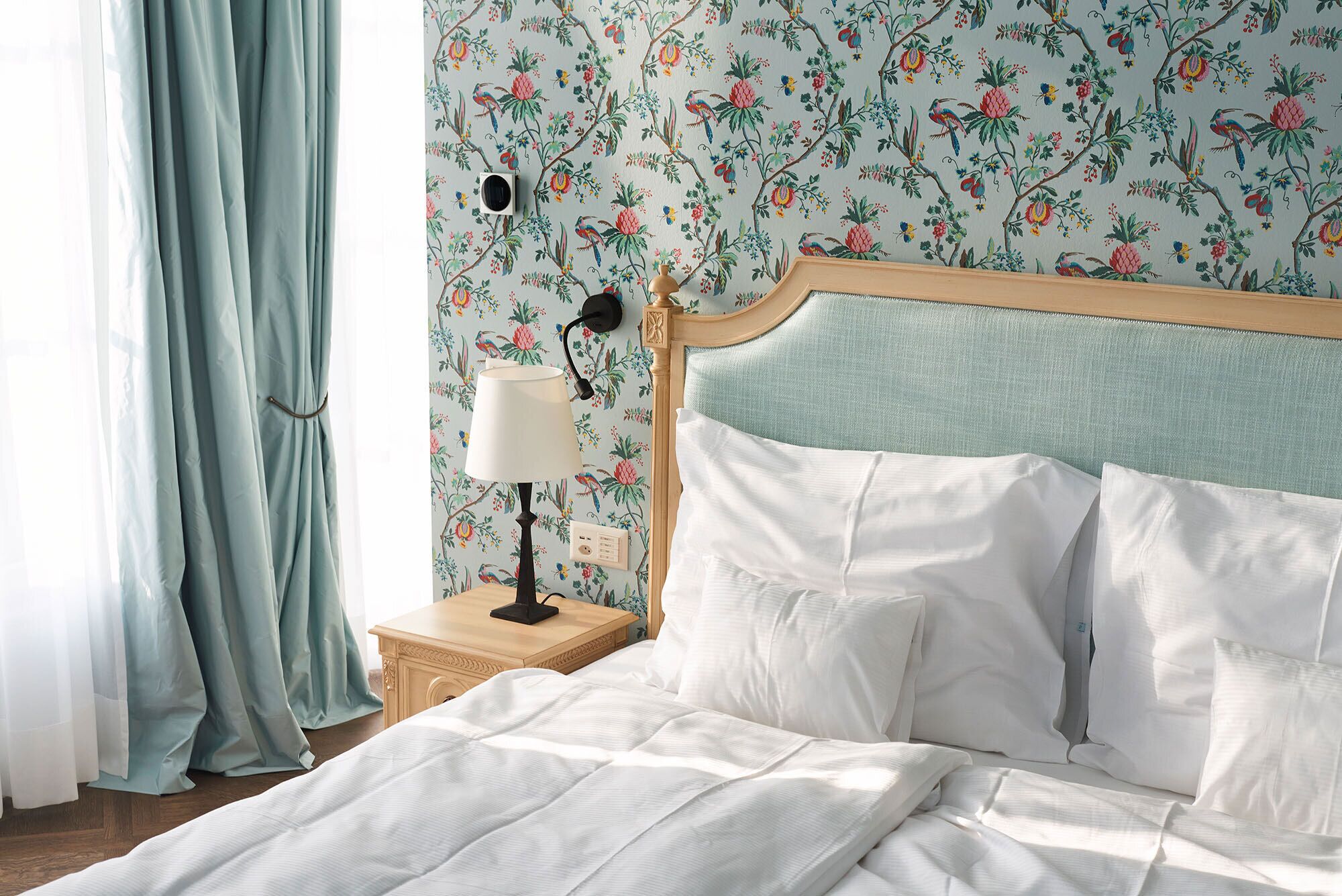 A neatly made bed with white linens, a wooden headboard, and a nightstand with a lamp and a small vase.