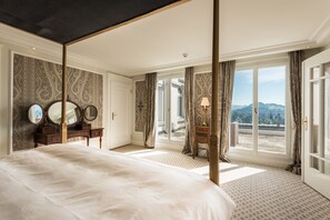 A spacious bedroom with a large bed, a vanity with mirrors, and a view of the outdoors through large windows.