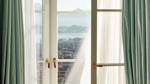 A view through a window with curtains, revealing a cityscape with buildings and a body of water. - Chateau Guetsch (Lucerne)