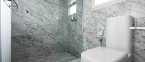 A bathroom with a marble floor and walls, a glass shower enclosure, and a white toilet.