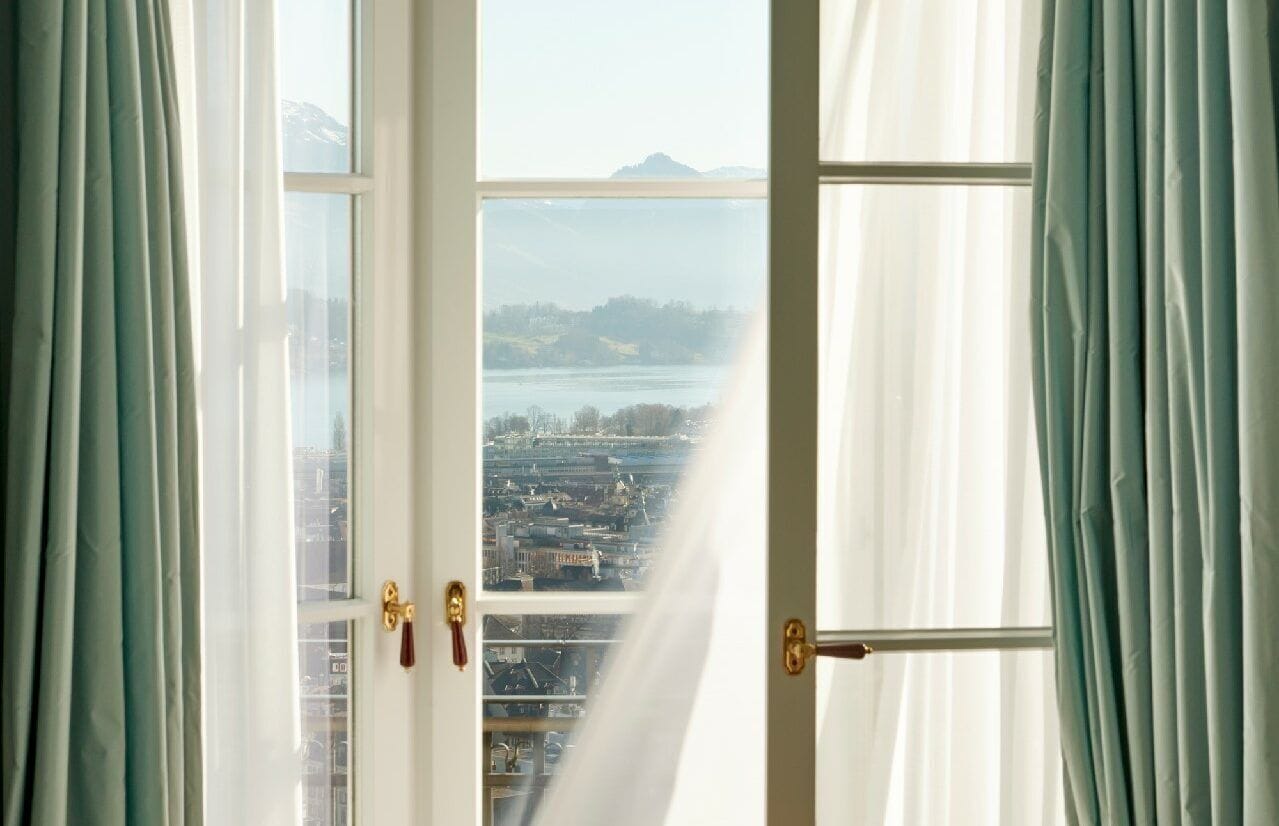 Una habitación con un ventanal, cortinas y vistas a la ciudad y montañas.