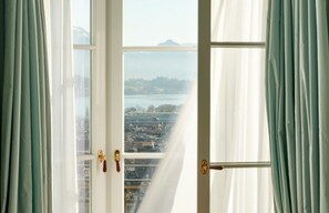 A room with a large window, curtains, and a view of a cityscape and mountains.