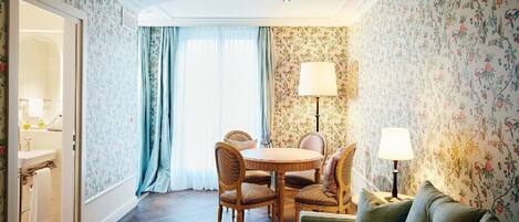 A room with a dining table, chairs, a sofa, a lamp, and a view through a window.