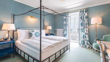A four-poster bed with white linens, a blue nightstand with a lamp, and a green chair.