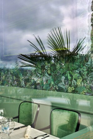 A restaurant with a tropical mural, green chairs, and a table set for dining.