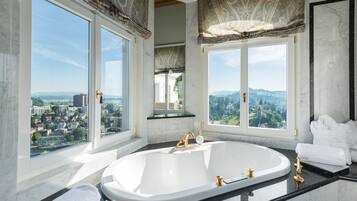 Un baño lujoso con una bañera independiente grande, encimeras de mármol y ventanas amplias con vistas a la ciudad.