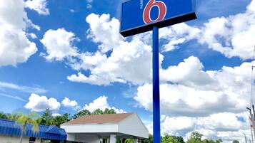A motel sign with the number 6, a gas station, and a building with a white roof.