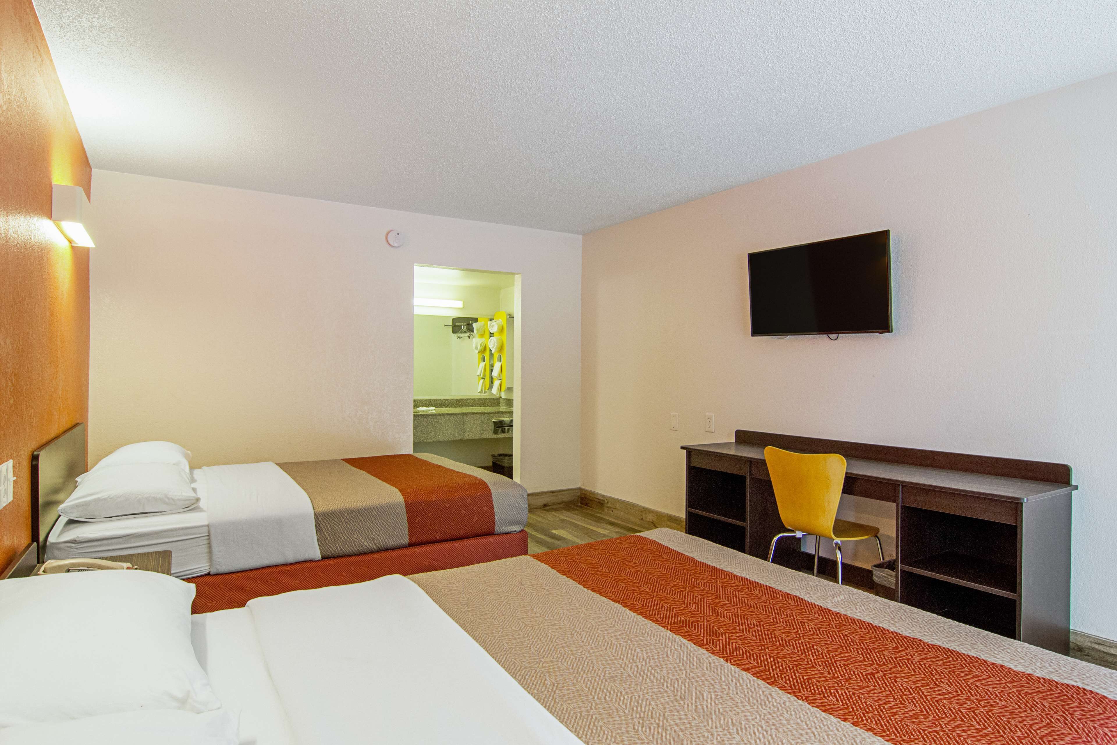 Camera d'albergo con due letti, una scrivania, una sedia, un televisore e bagno visibile tramite una porta aperta.