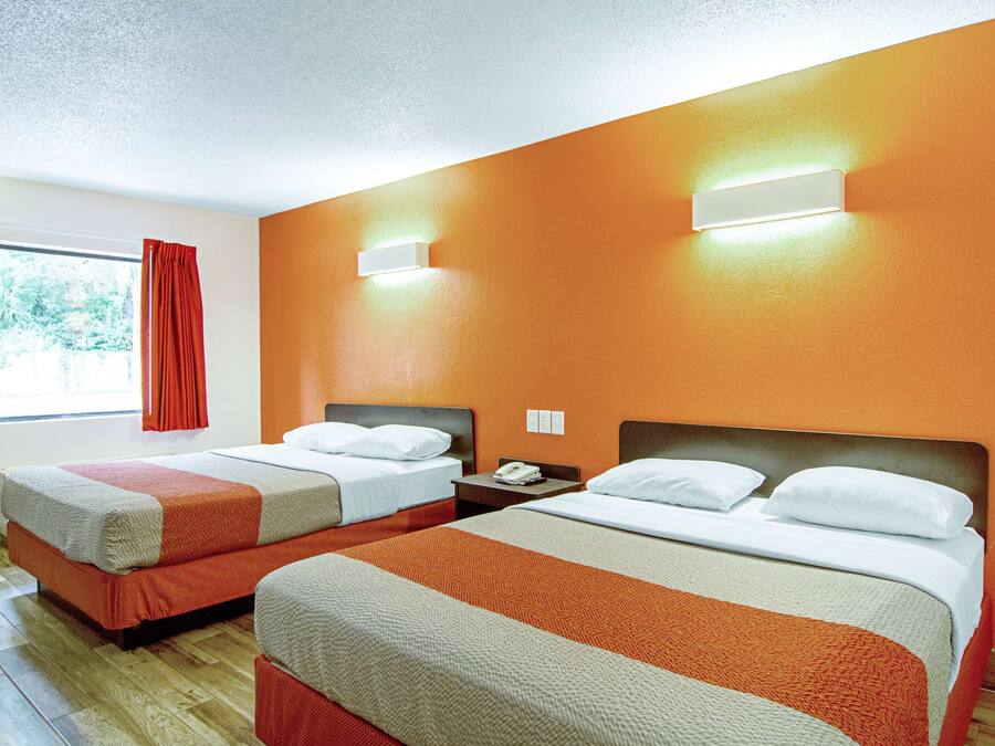 Habitación de hotel con dos camas, una ventana con cortinas rojas y una lámpara fijada a la pared.