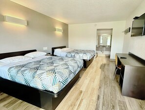 Ein Hotelzimmer mit zwei Betten, einem Schreibtisch und einem durch eine geöffnete Tür einsehbaren Badezimmer.