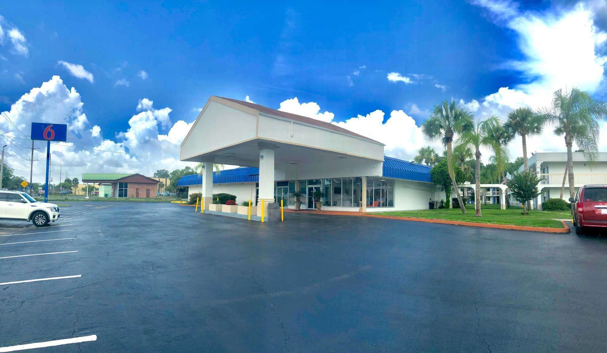 A gas station with a covered fuel pump area, a parking lot, and palm trees in the background.