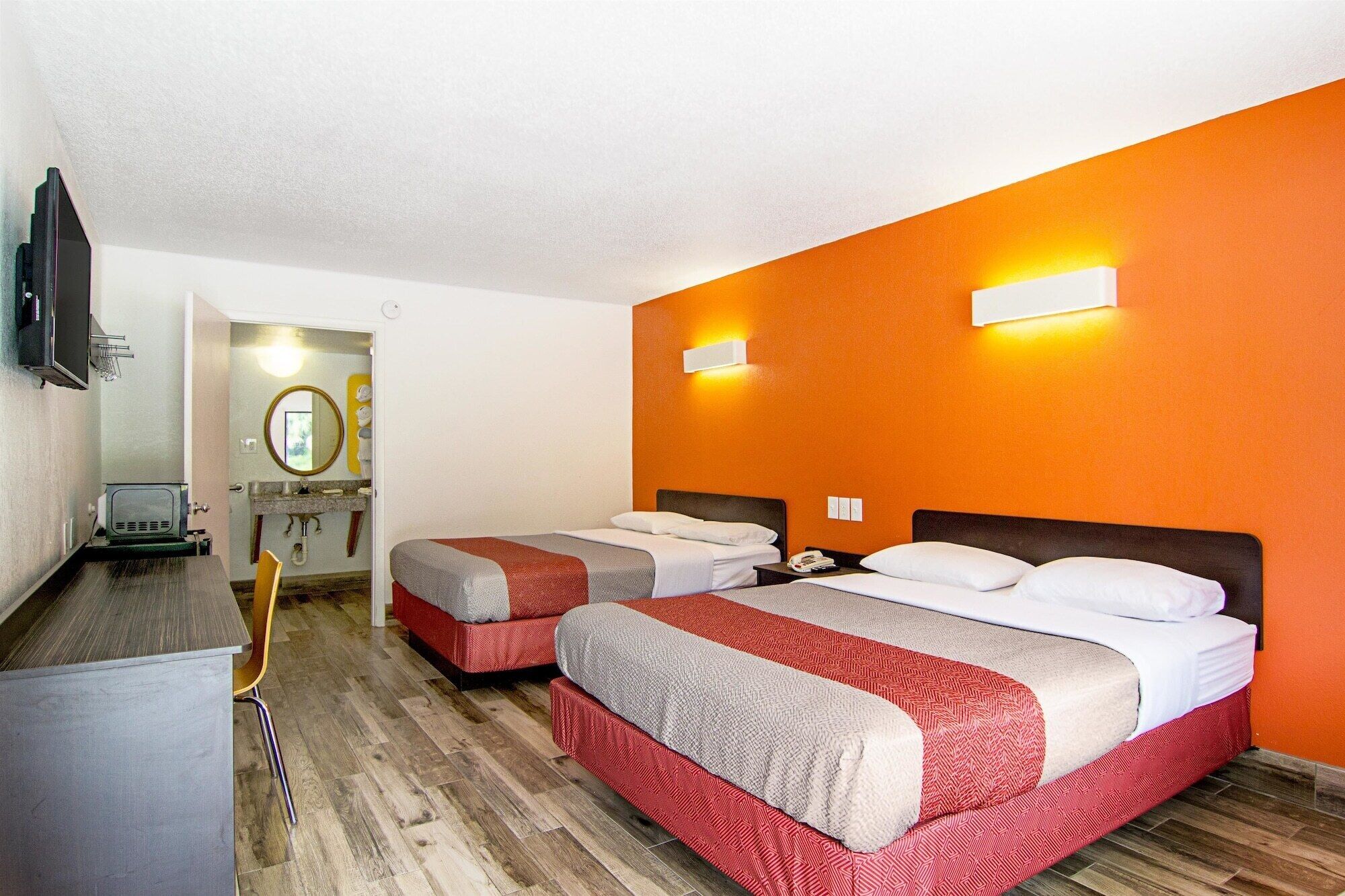 Habitación de hotel con dos camas, un escritorio, un televisor y un baño visible a través de una puerta abierta.