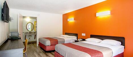 Habitación de hotel con dos camas, un escritorio, un televisor y un baño visible a través de una puerta abierta.