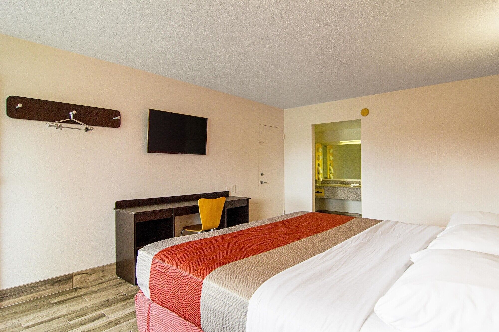 A hotel room with a bed, a desk, a chair, a TV, and a mirror.