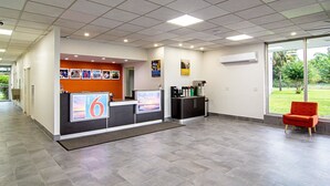 A hotel reception area with a modern design, featuring a reception desk, a coffee station, and a view of the outdoors. - Motel 6 Starke, FL (Starke)