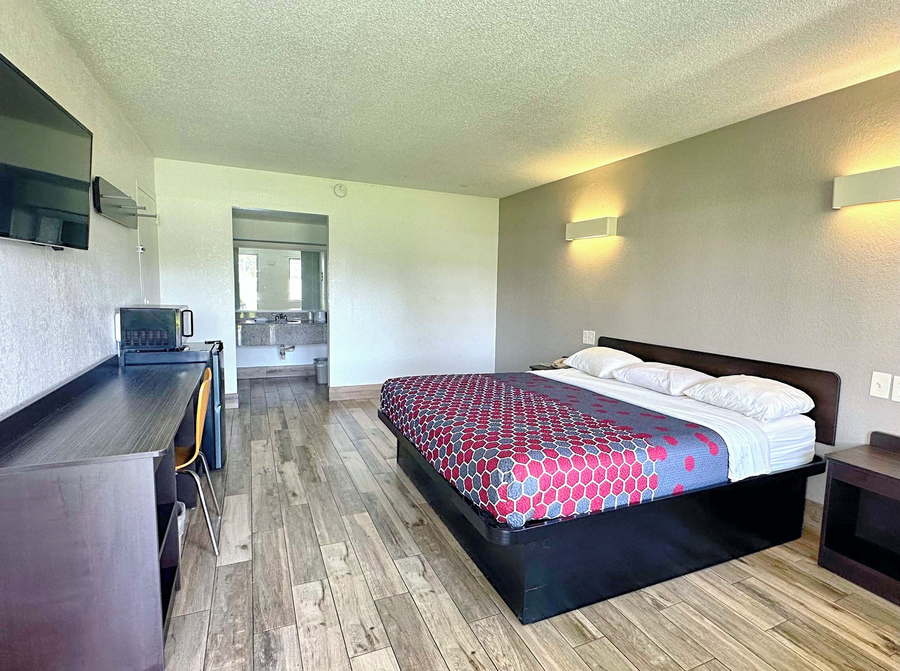 A hotel room with a bed, a desk, a chair, a television, and a bathroom visible through an open door.