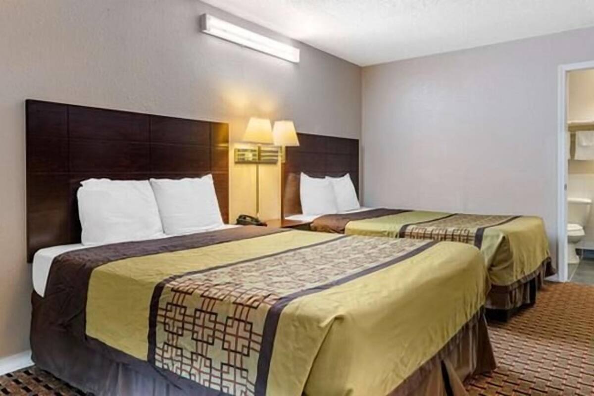 A hotel room with two beds, each with a headboard, a bedside lamp, and a patterned bedspread.