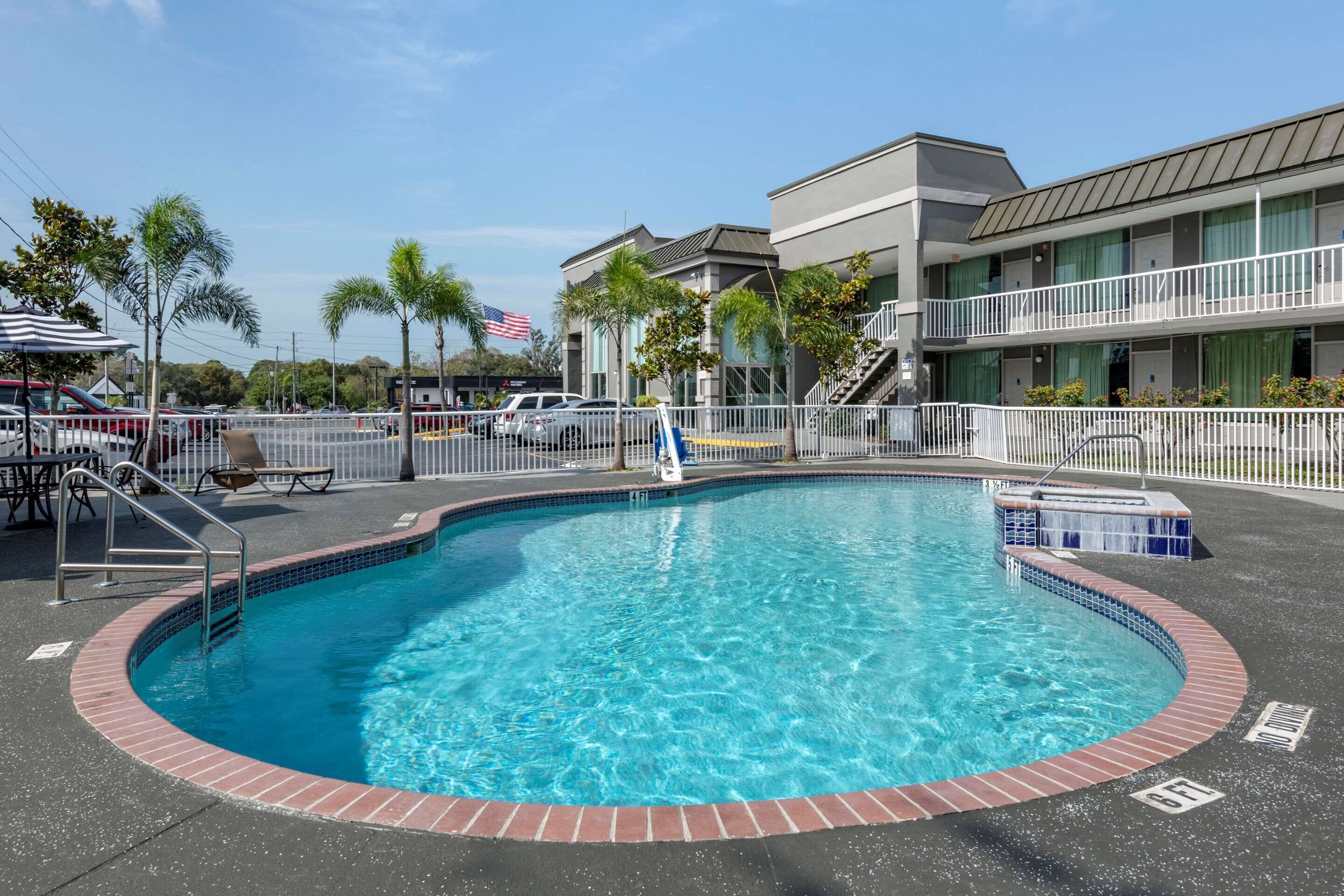 A swimming pool with a brick border, surrounded by a fence, and adjacent to a building with a balcony.