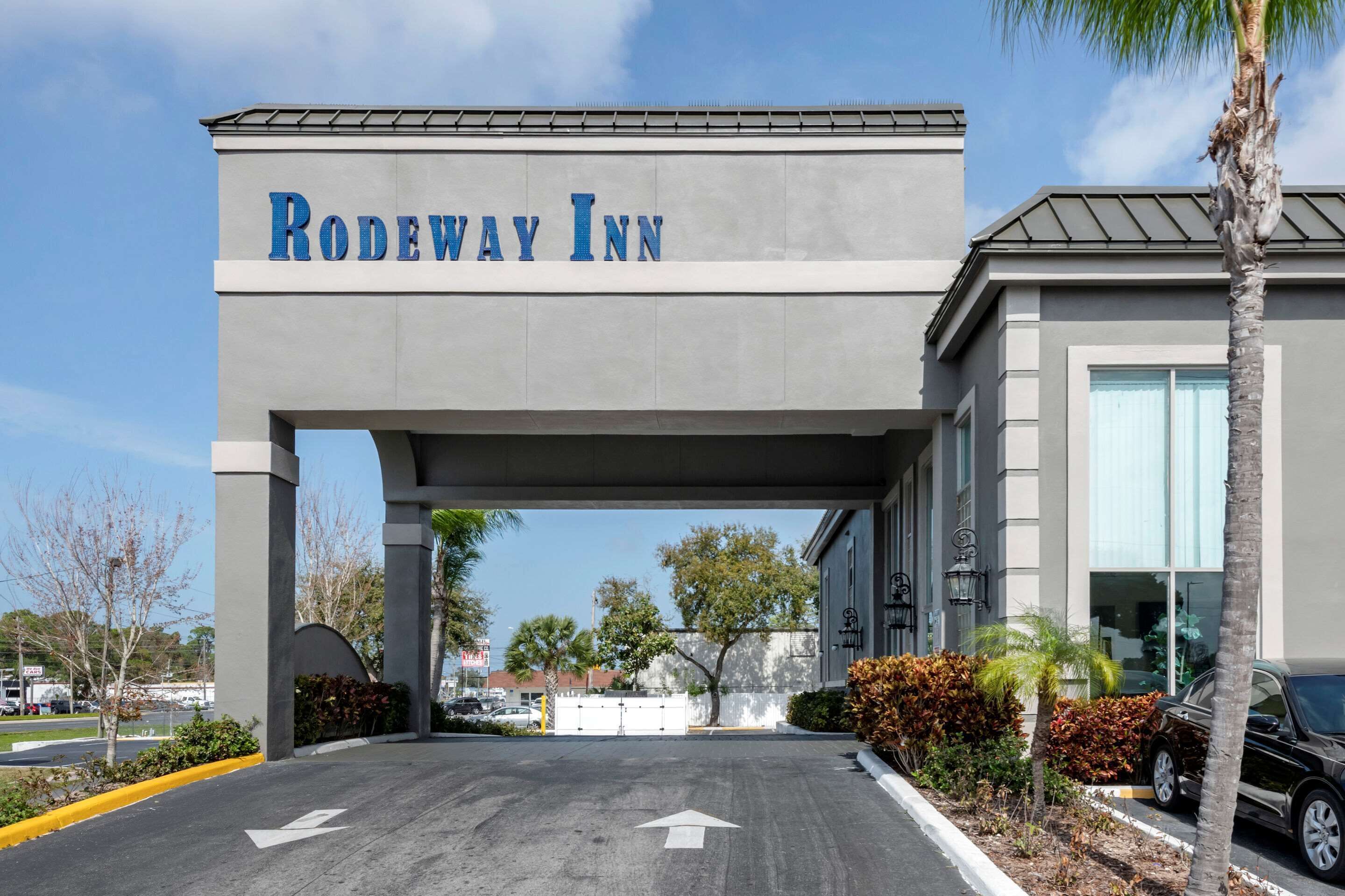 La entrada al Rodeway Inn, con un letrero visible sobre la puerta, un estacionamiento con flechas indicativas y la fachada del edificio con grandes ventanales.