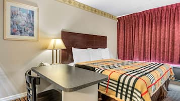 Habitación de hotel con cama, escritorio, silla, lámpara y un cuadro en la pared.