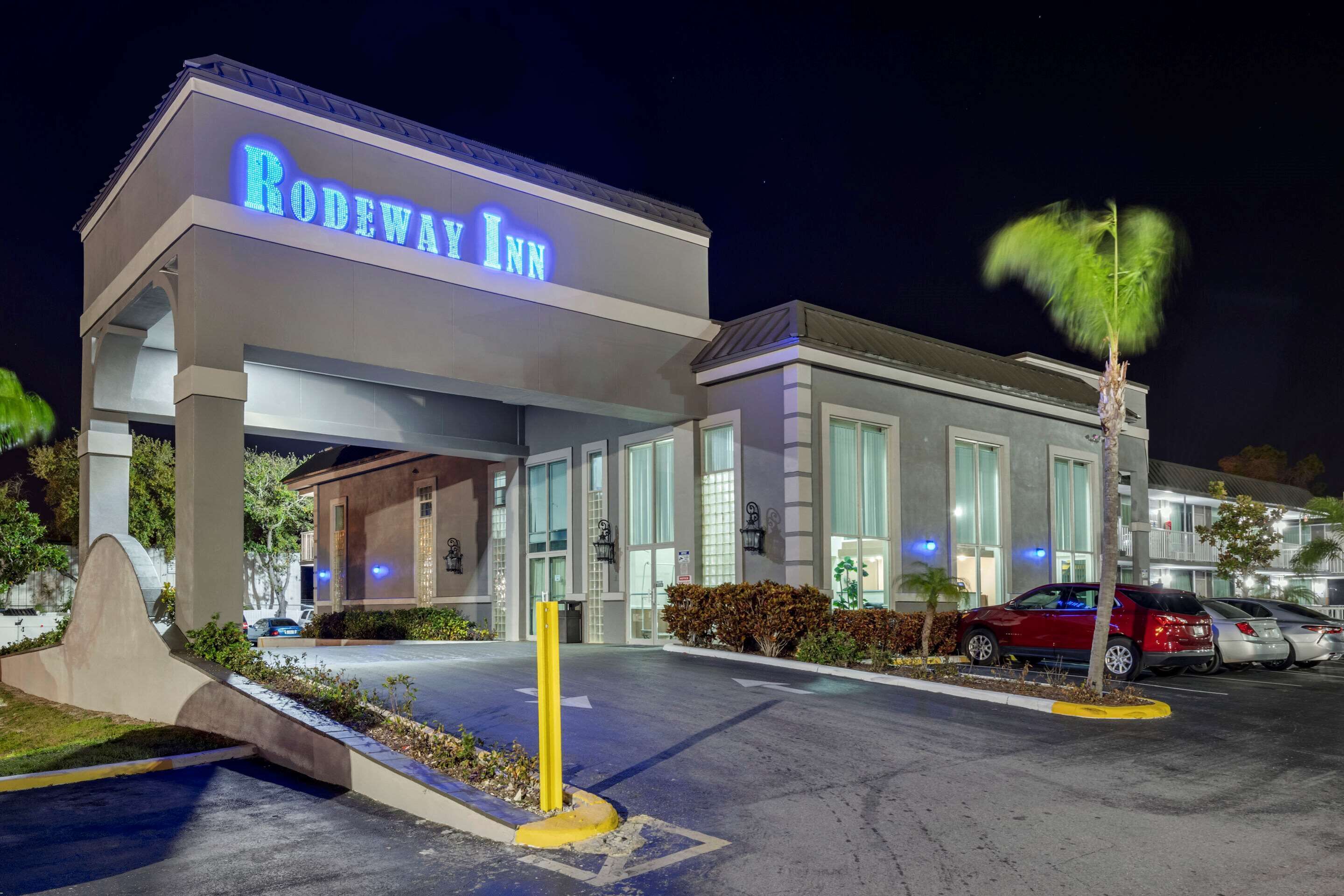 The exterior of the Rodeway Inn hotel with a modern design, large windows, and a parking area with cars.