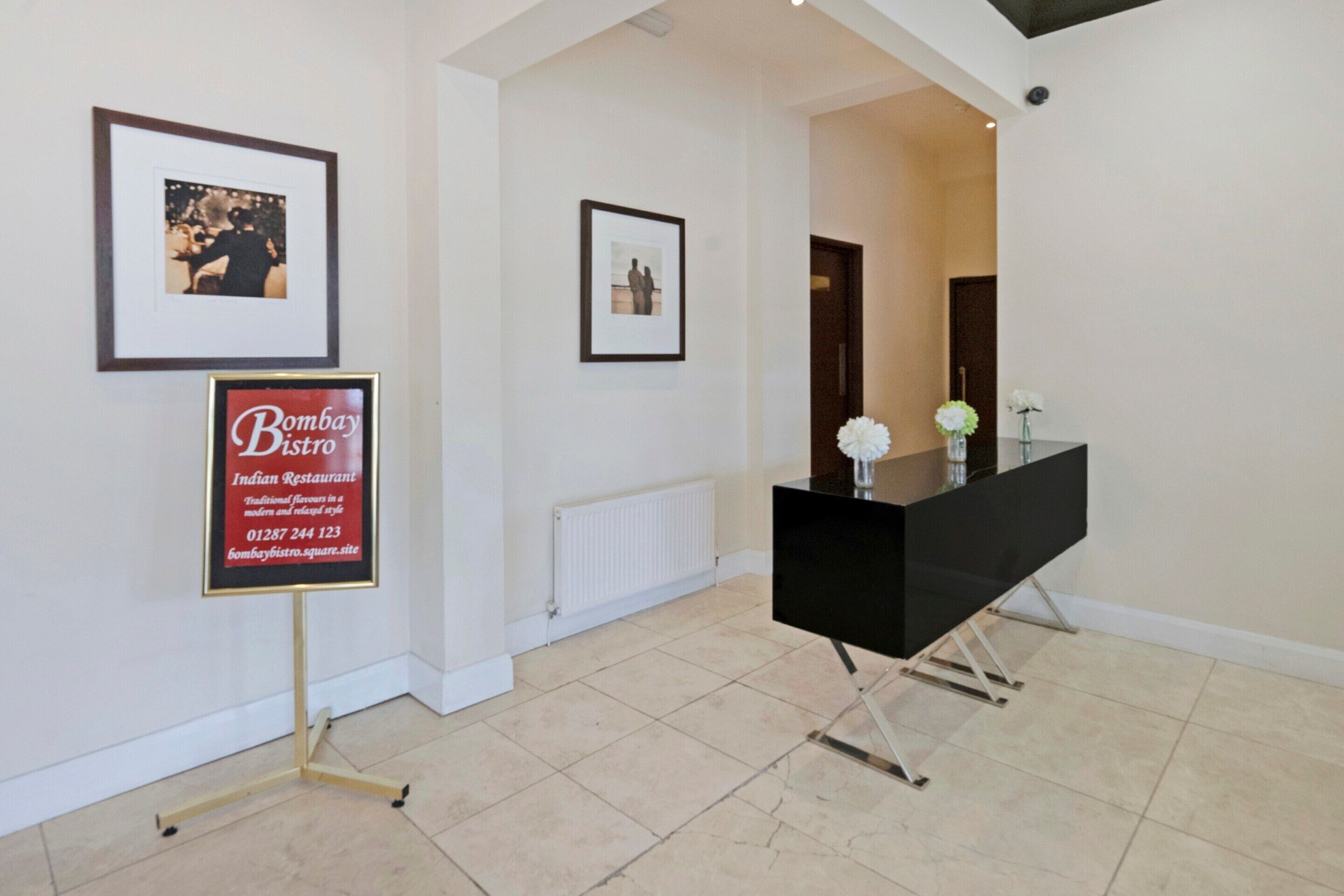 A hallway with framed pictures on the walls, a black reception desk, and a white tiled floor.