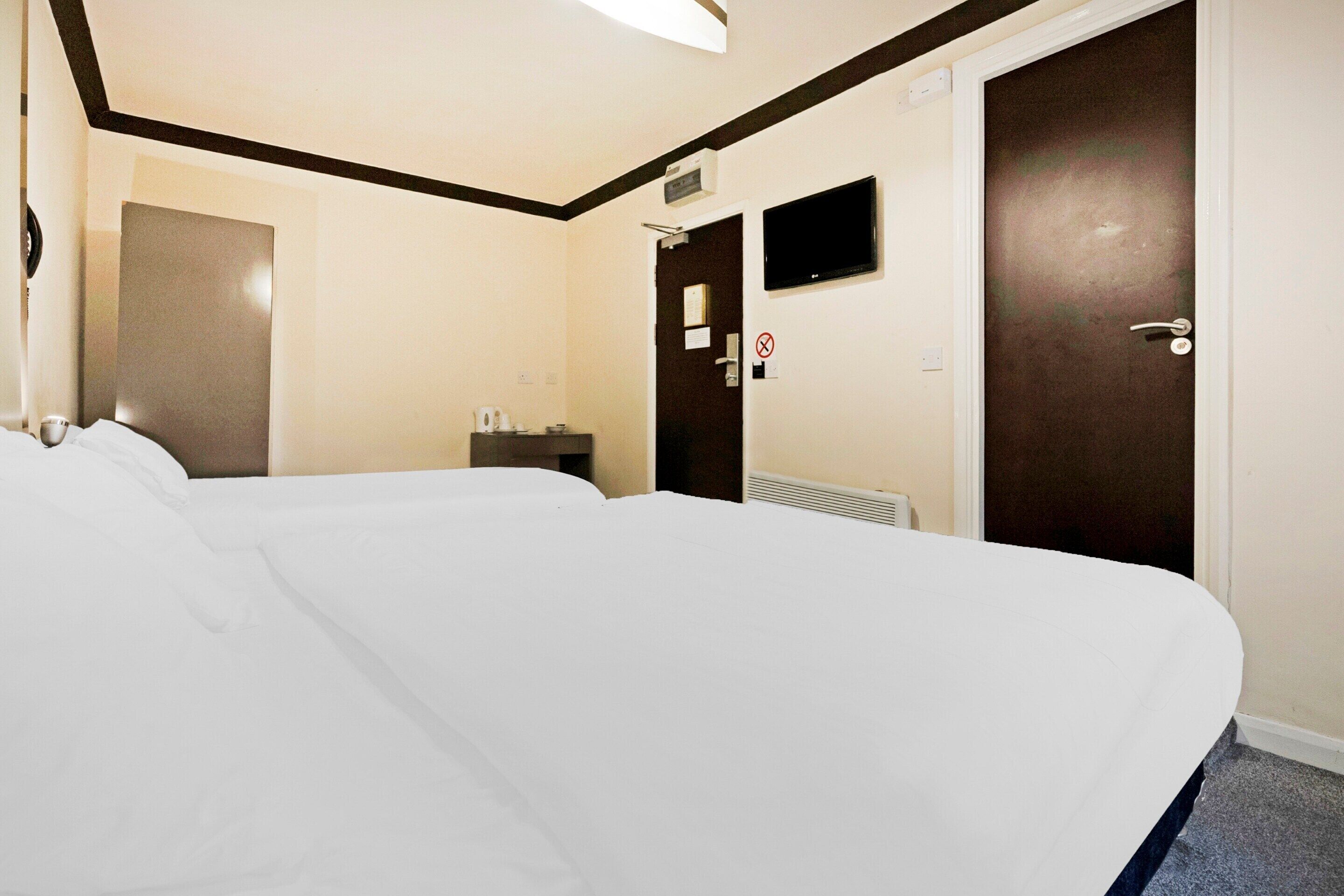 A hotel room with a large bed, a desk, a chair, a television, and a door.