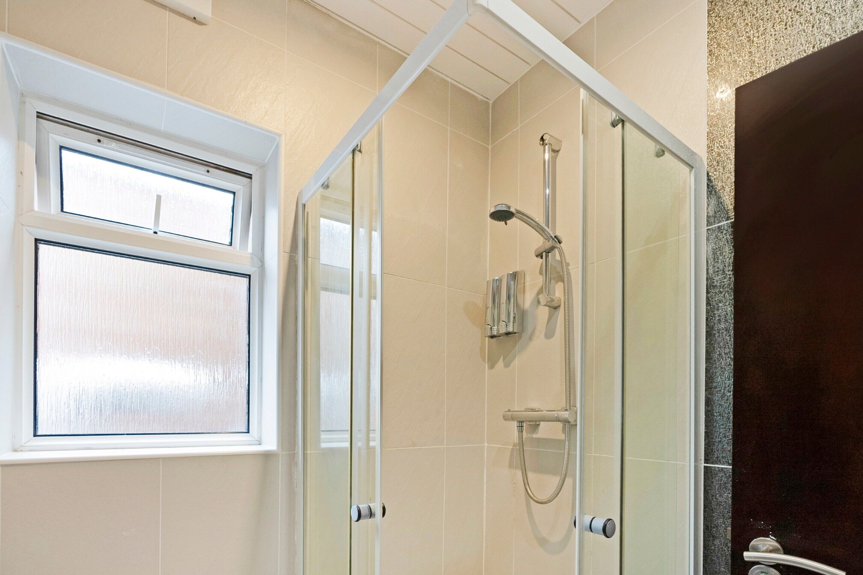A glass-enclosed shower area with a handheld showerhead and a wall-mounted faucet.