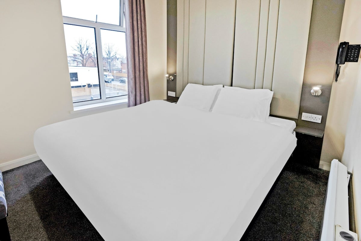 Ett hotellrum med en stor säng, ett fönster, en telefon och ett element.