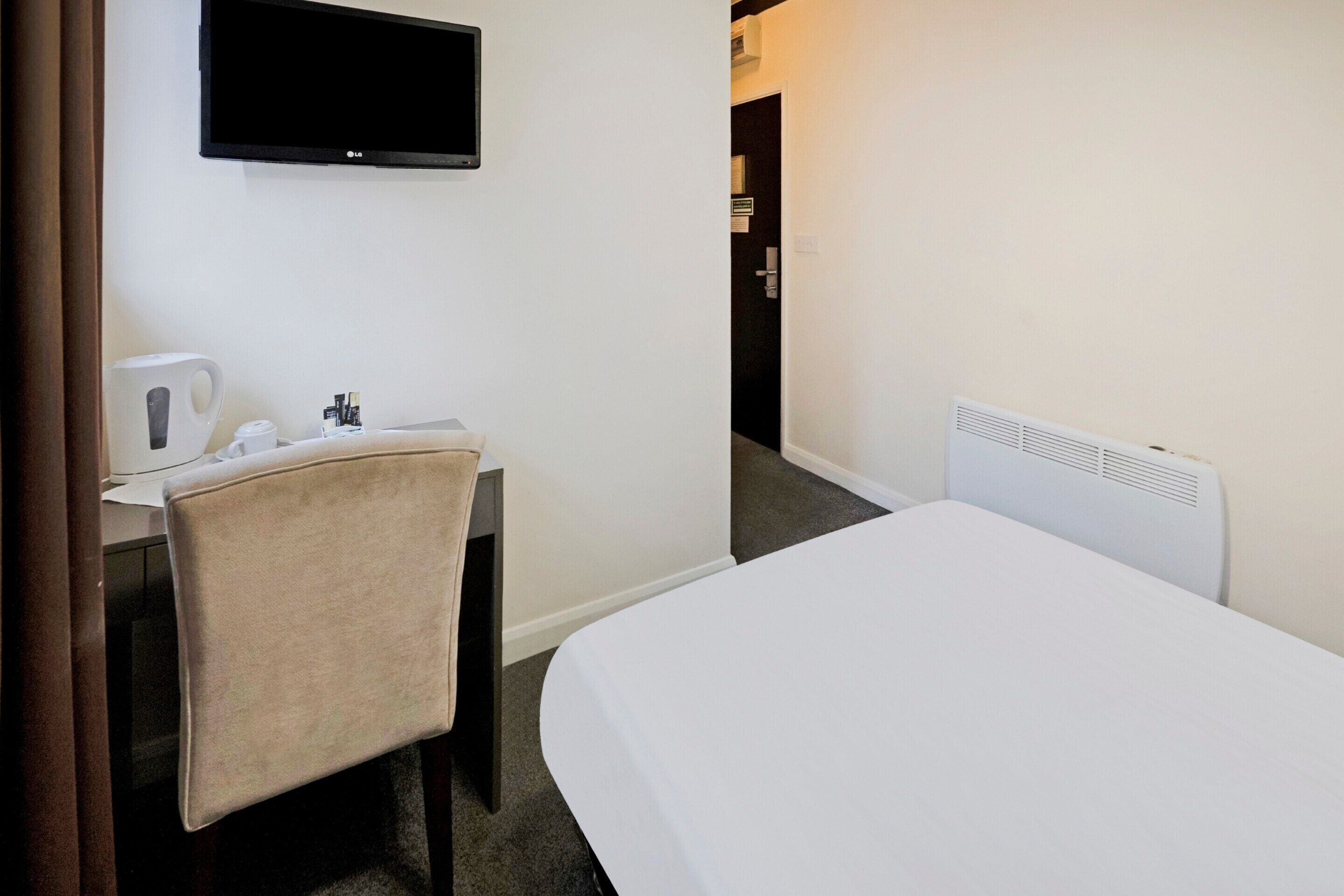 Ett hotellrum med en säng, ett skrivbord med en stol, en tv och ett element.