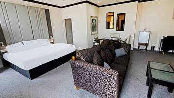 A modern hotel room with a large bed, a patterned sofa, a glass coffee table, and a desk with a chair.