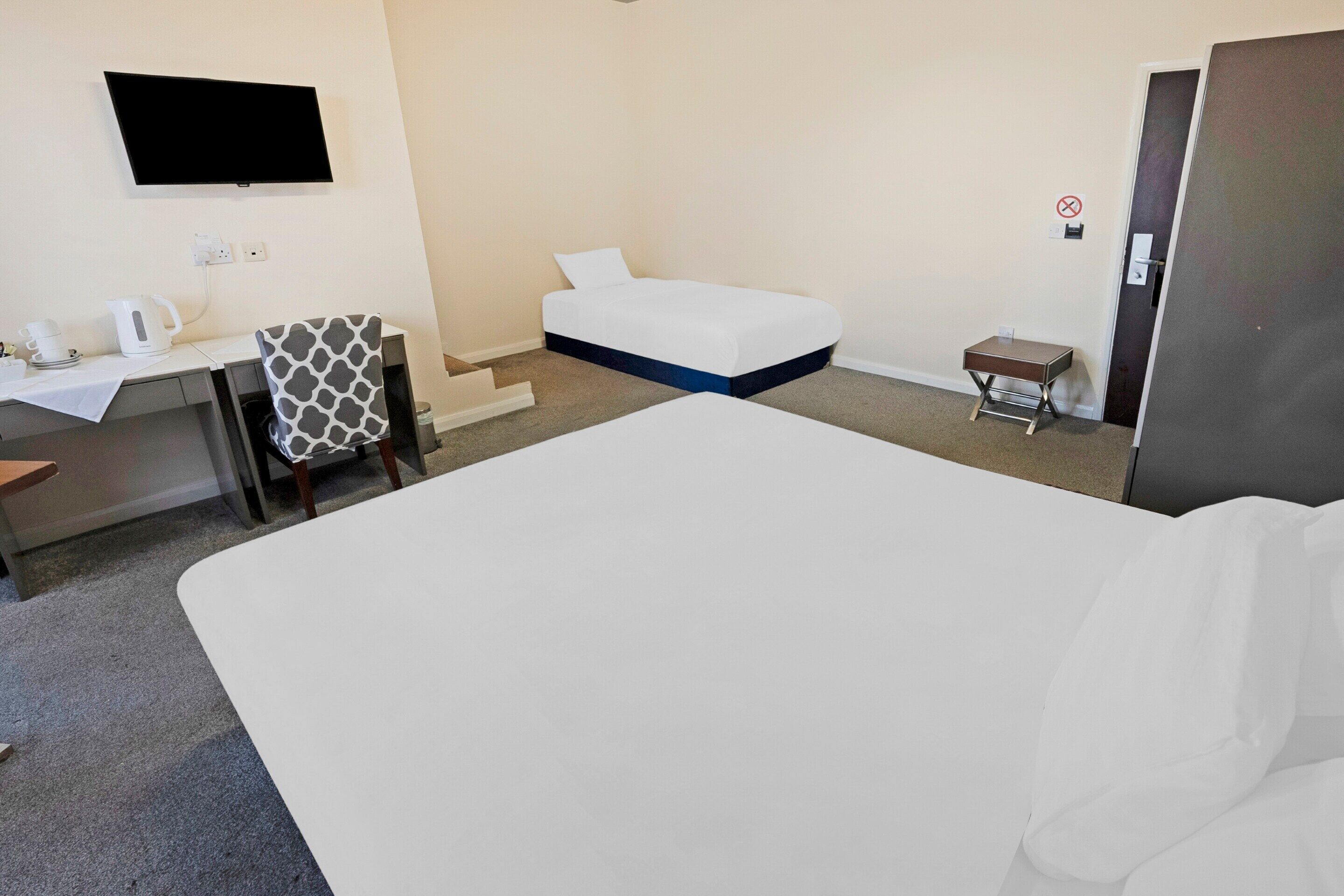 A hotel room with a bed, a desk with a chair, a television mounted on the wall, and a small table with a chair.