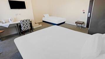 A hotel room with a bed, a desk with a chair, a television mounted on the wall, and a small table with a chair.