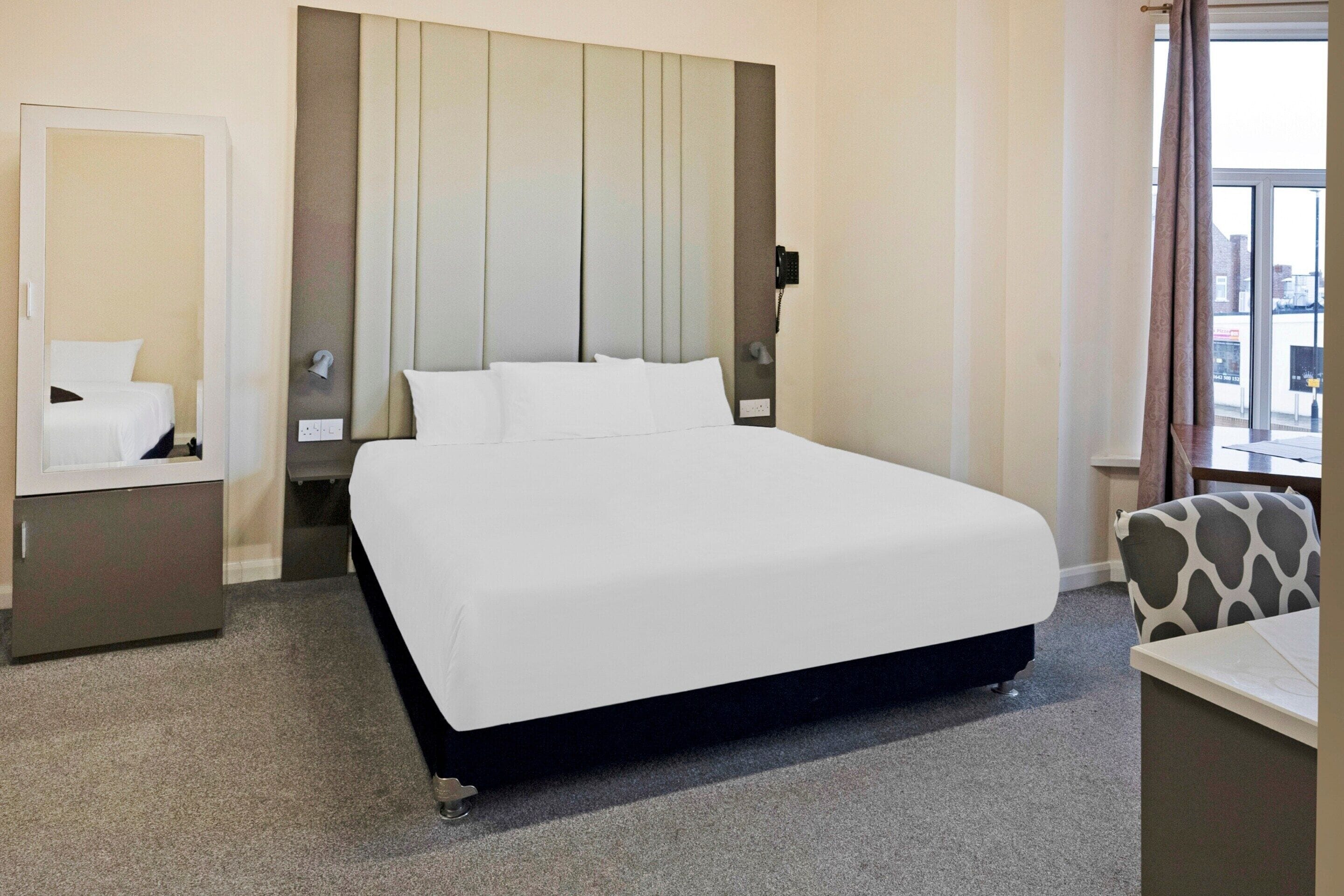 Une chambre d’hôtel avec un grand lit, une table de chevet, une chaise et une fenêtre donnant sur la ville.