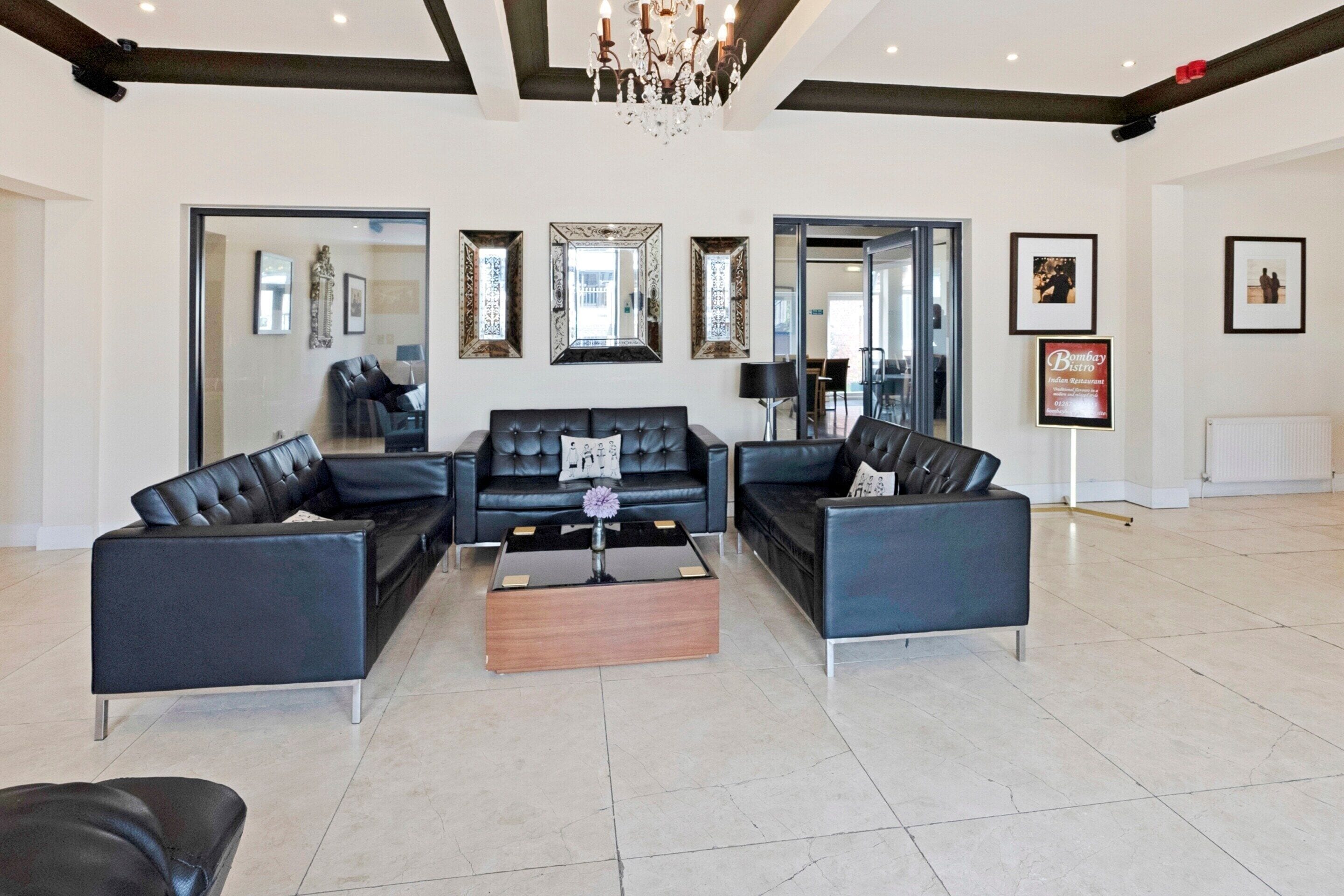 A spacious living area with a black leather sofa set, a wooden coffee table, and a chandelier.