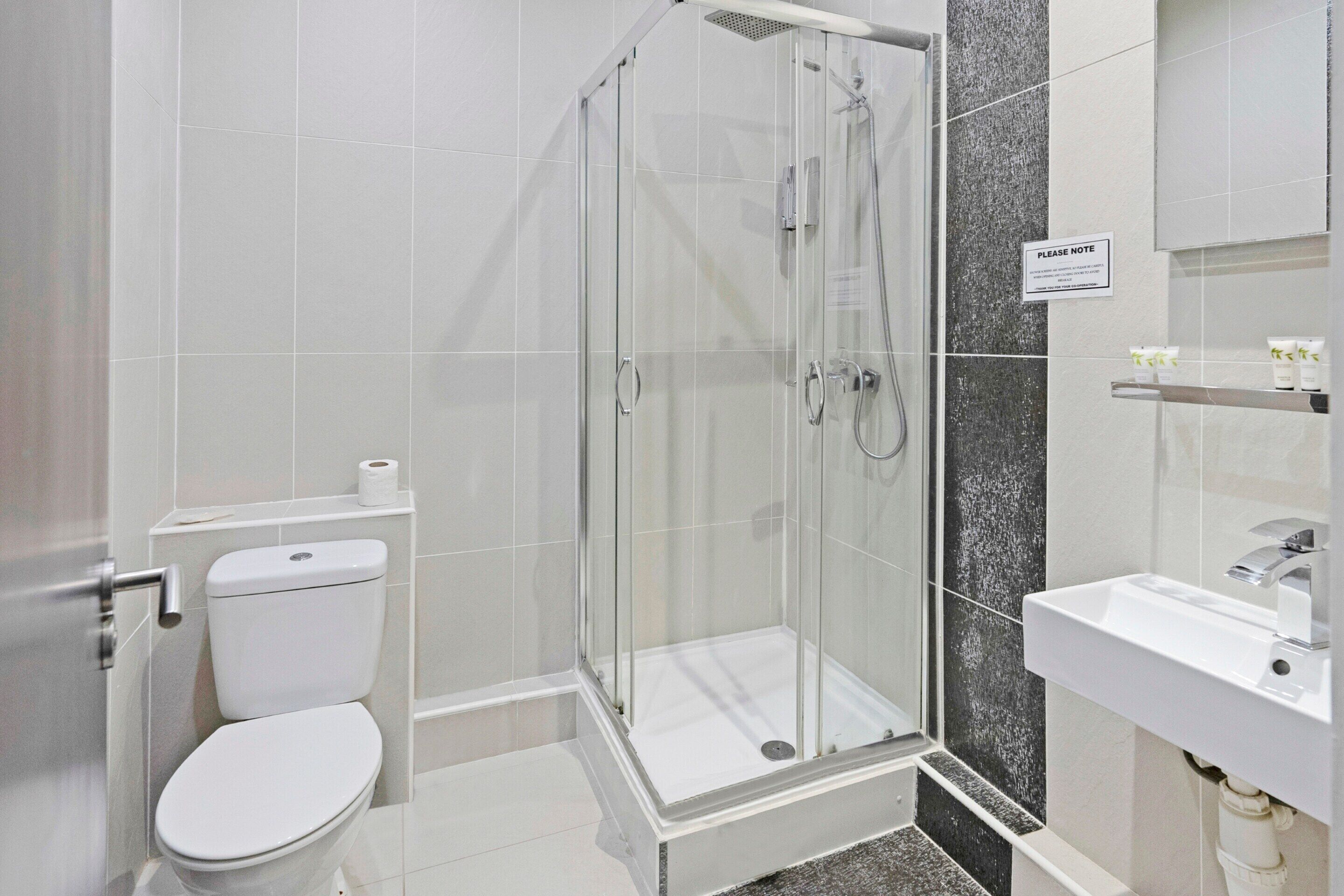 A modern bathroom with a glass-enclosed shower, a white toilet, and a sink with a mirror.