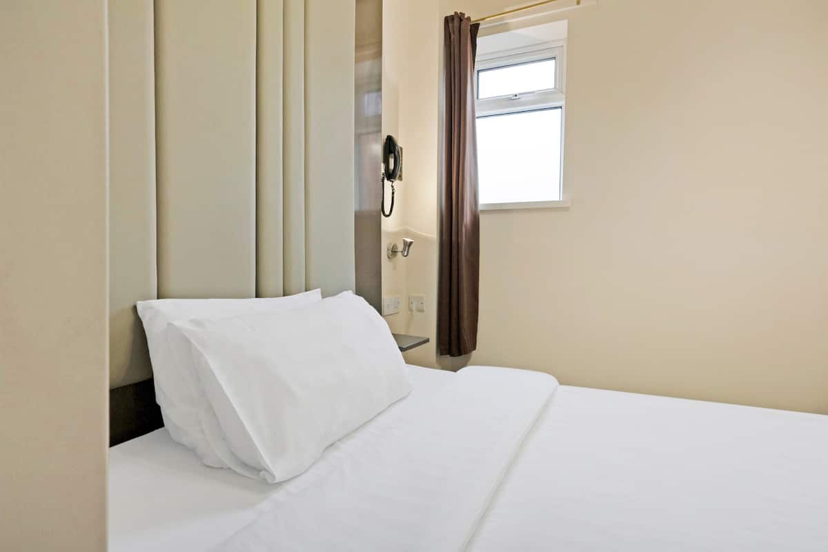 Ett hotellrum med en säng, en telefon och ett fönster med gardiner.