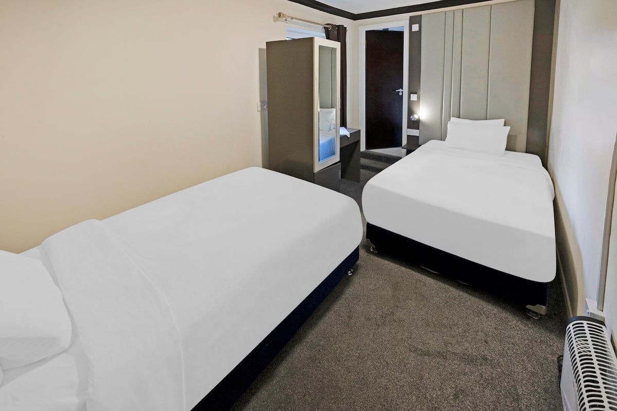 Ett hotellrum med två sängar, en spegel, en dörr och en värmare.