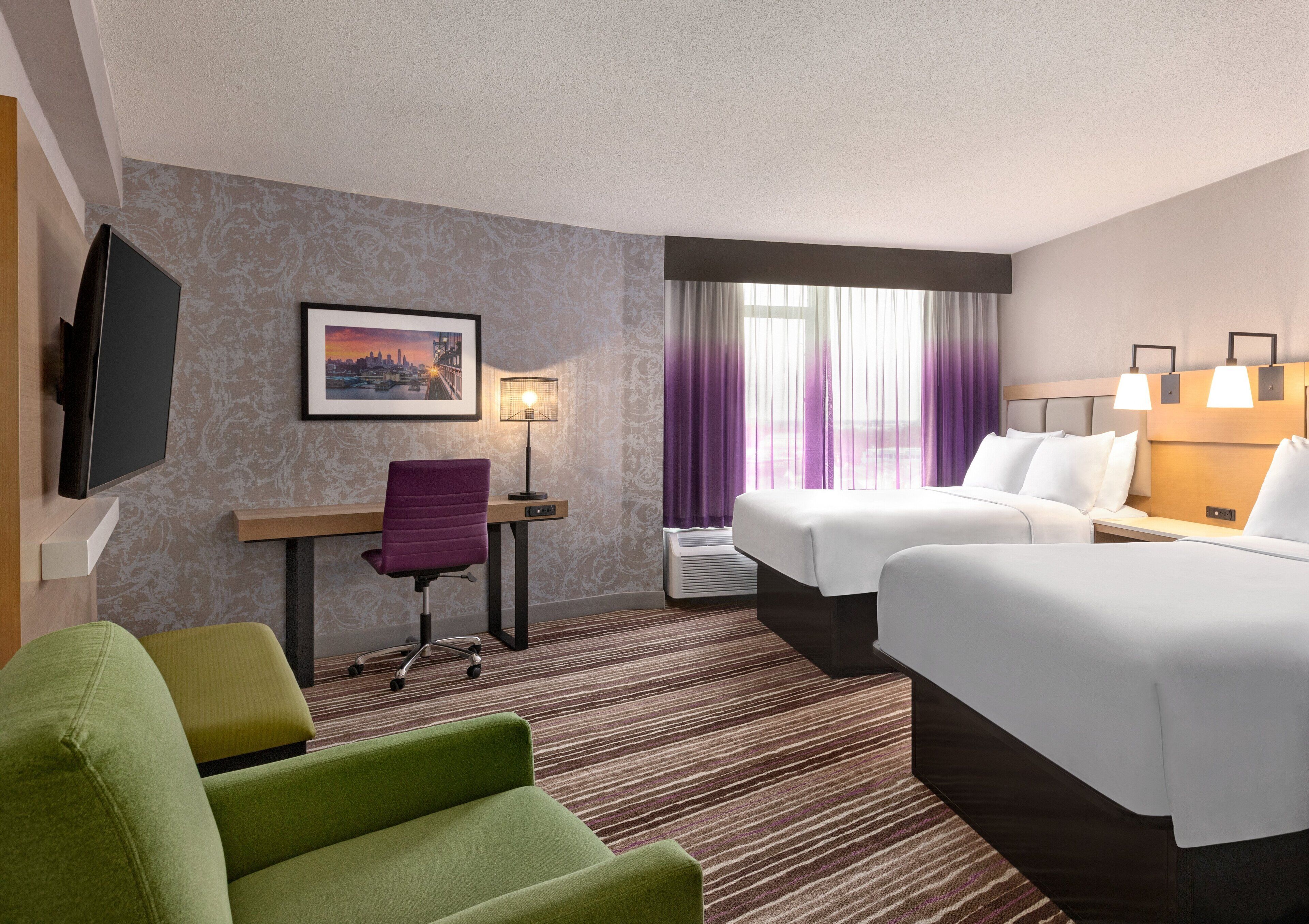 A hotel room with two beds, a desk, a chair, a TV, and a window with curtains.